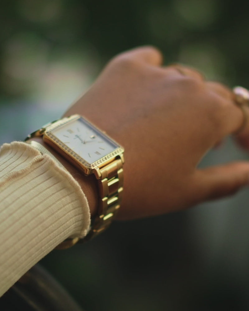 A square womens watch in 22k gold-plated 316L stainless steel with stones from WALDOR & CO. with black sunray dial and a second hand. Seiko VJ22 movement. The model is Delight 32 Mayfair 28x32mm. 